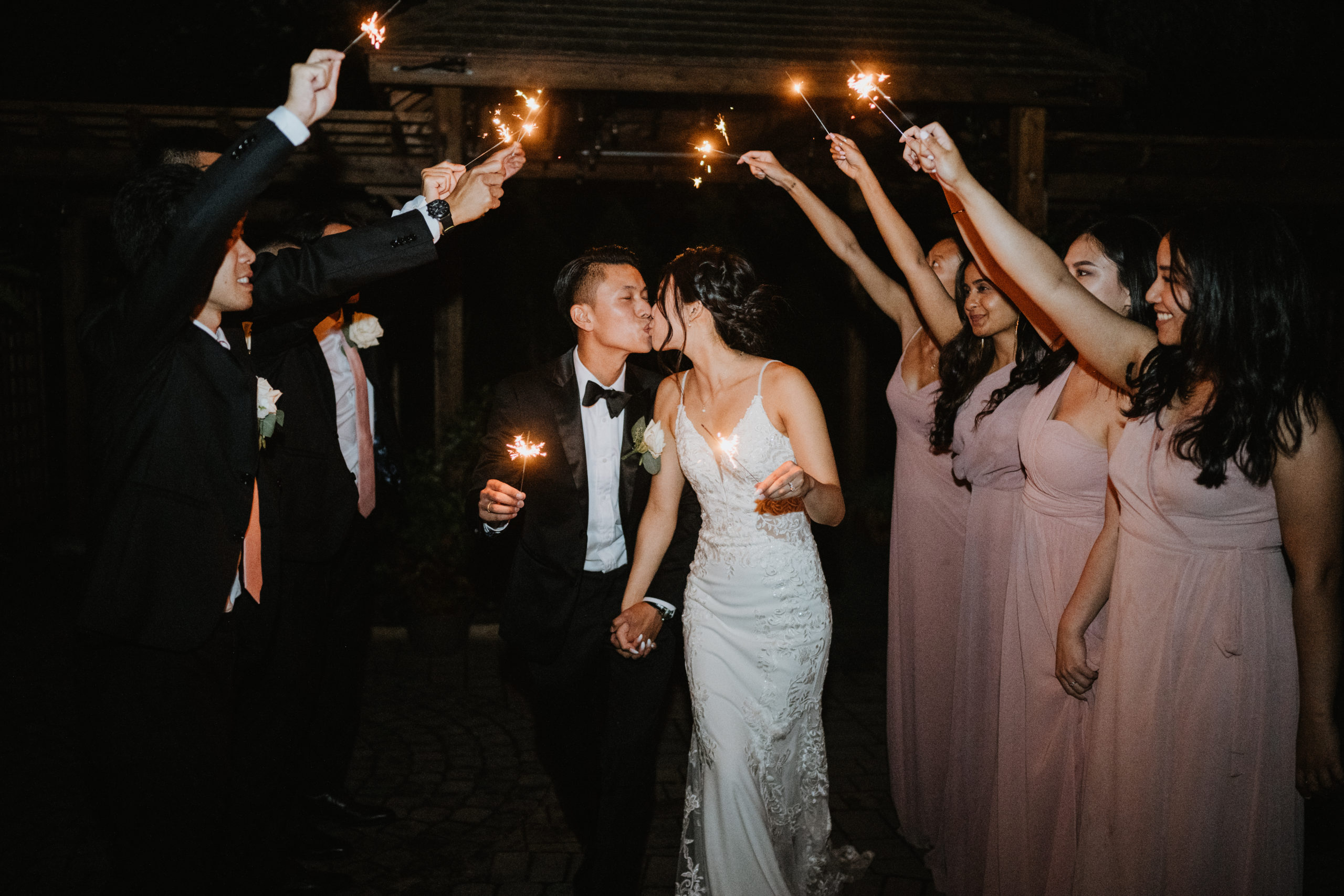 Billy and Petrina kissing on the dance floor while their friends hold sparklers above their heads