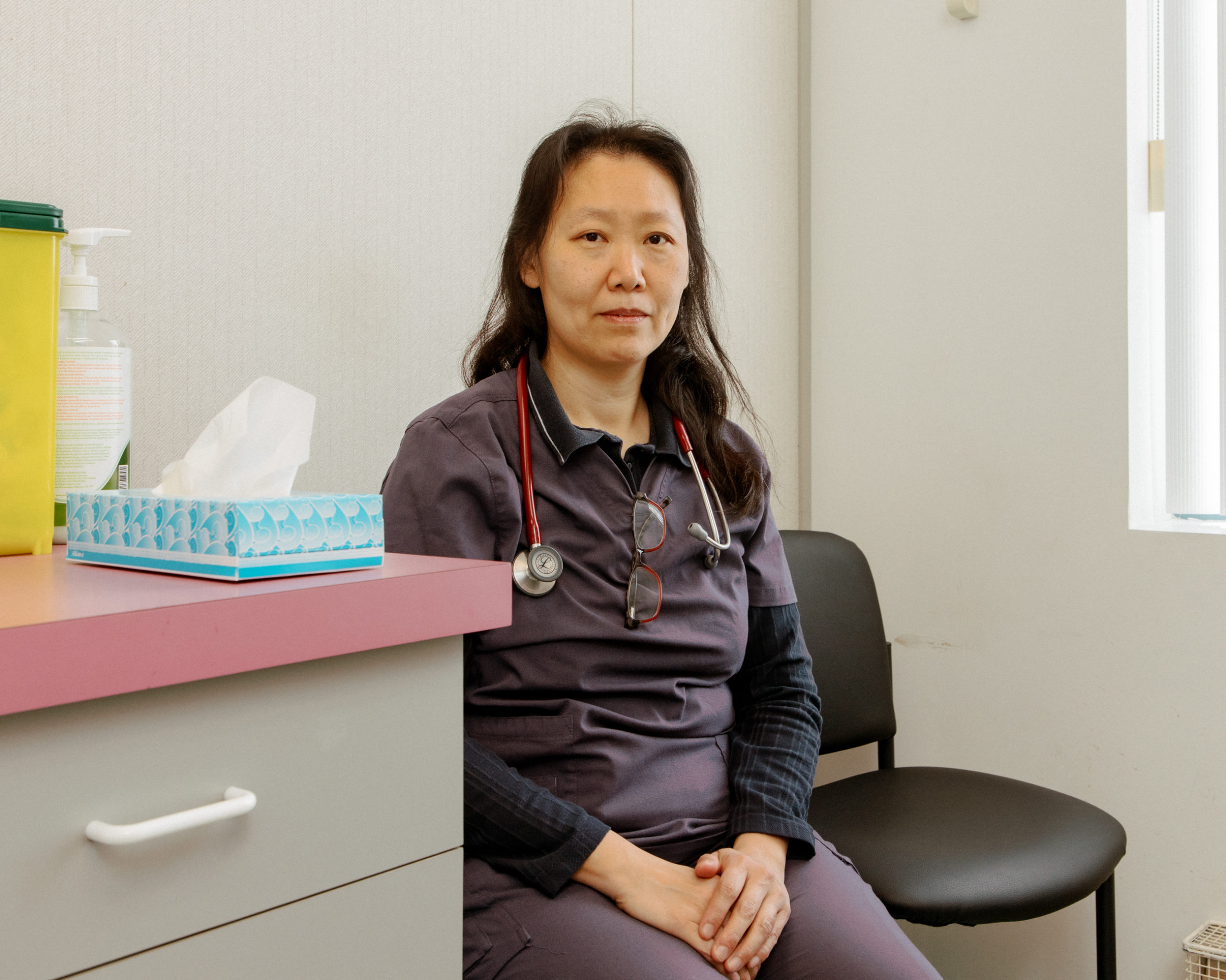 Fan.Wah Mang, a family doctor who's closing her practice, sits in her scrubs in one of her exam rooms
